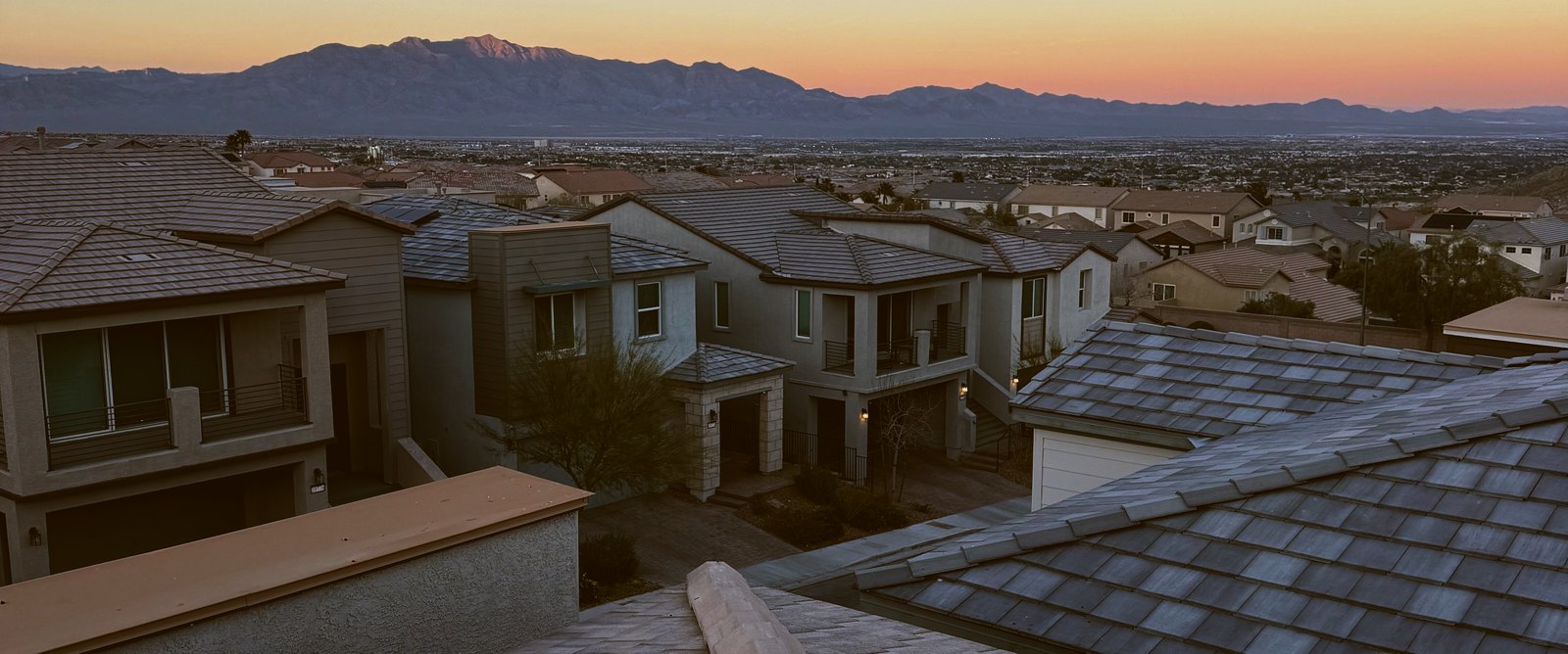 Tile rooftops of a desert subdivision at dusk, with mountains along the horizon