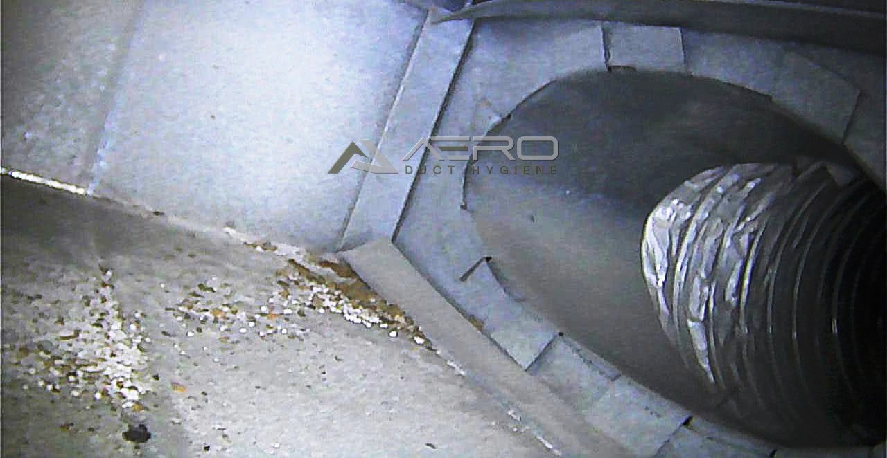 A main supply duct before cleaning, with debris gathered around the duct connection
